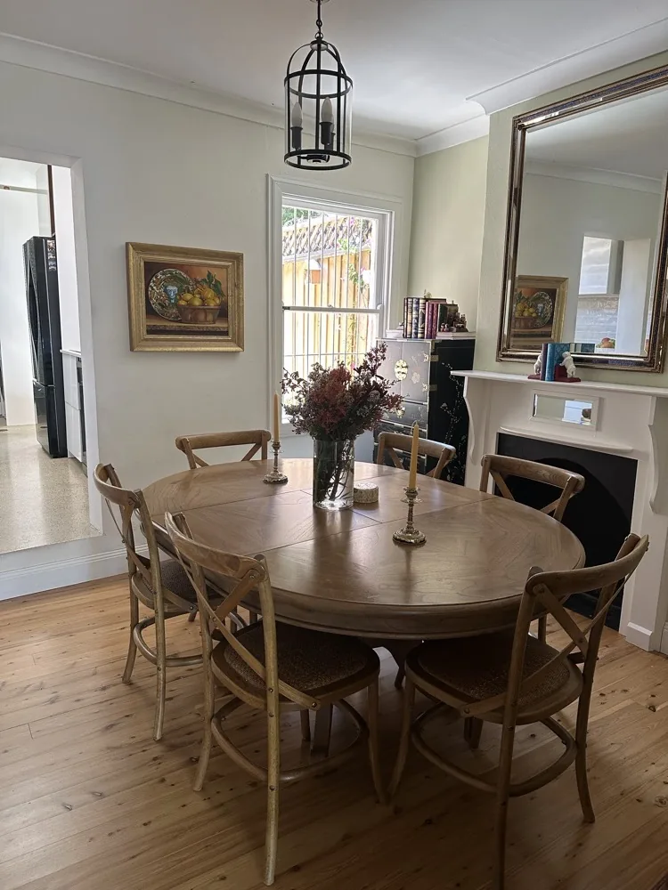 Our dining room with a round timber table, an old painting and a gilt mirror over the fireplace